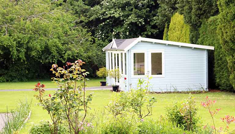 Quaint light-blue summer house with large windows, situated in a landscaped garden and lawn.