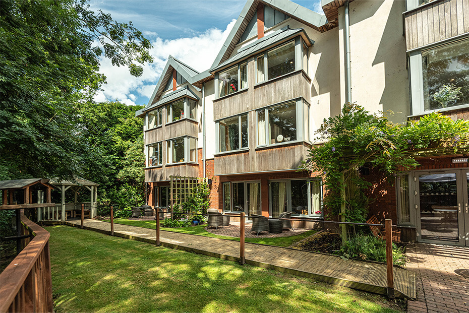 Multi-story building with a combination of wooden and white exteriors, surrounded by lush greenery and a well-maintained and landscaped garden