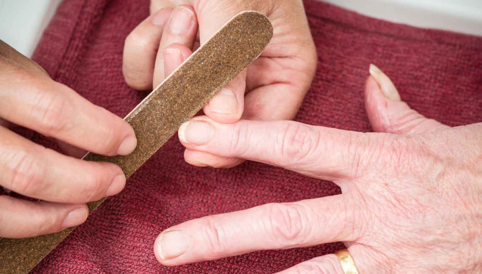 Close-up of a person filing another person's fingernails with a brown nail file