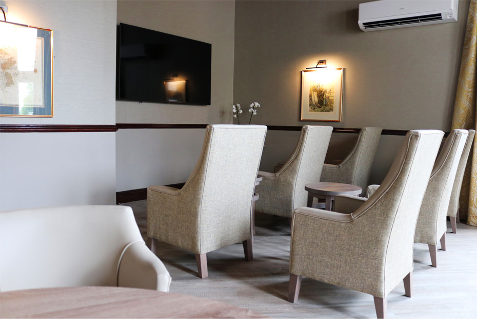 A lounge and theatre room with cream upholstered chairs, a wooden table, and wall-mounted television