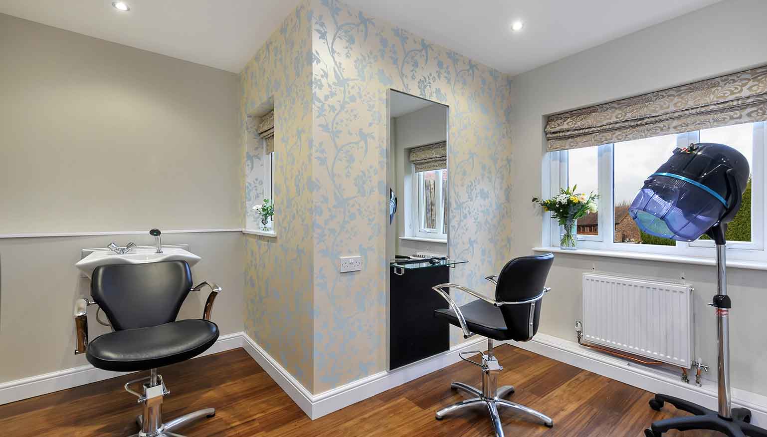 A modern hair salon with two black styling chairs in front of a large mirror and a window providing natural light