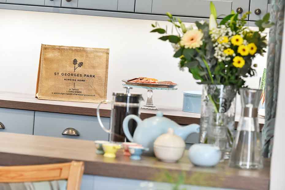 Kitchen countertops with a bouquet of flowers, and various kitchen items. A bag with the text 'St George's Park' is visible in the background
